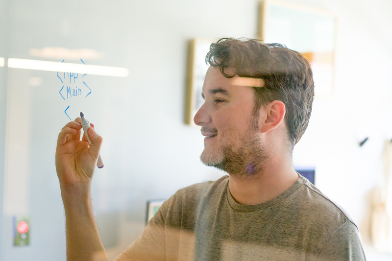 一位面带微笑的男子用干记号笔在玻璃墙上写了一个应用程序结构示例。